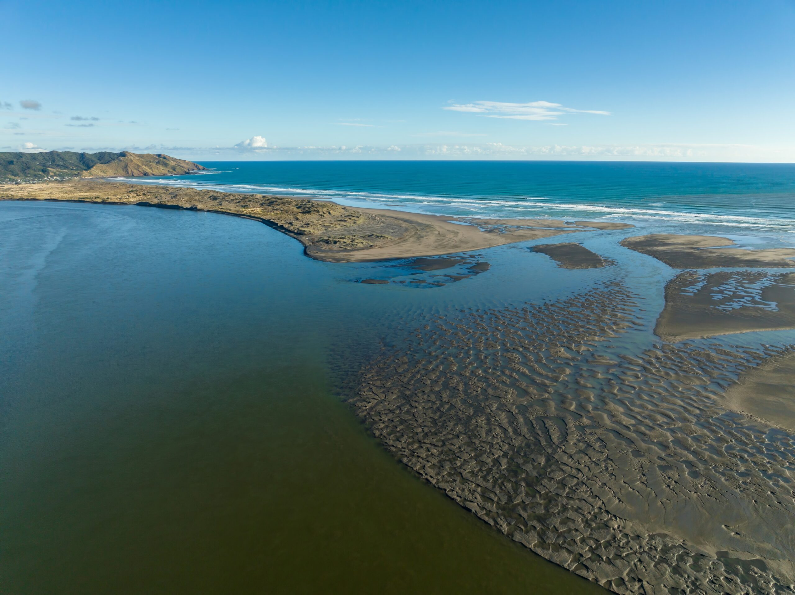 aerial view of a tidal estuary meeting the ocean. low tide reveals intricate patterns in the mudflats. coastal landscape. waikato river, port waikato, waikato, new zealand